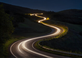 Winding curvy rural road with light trail from headlights leading