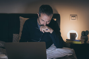 Tired man on bed after hard works with laptop until late at night. Bored boy sitting in bedroom use online devices. Smart working, home school, internet lifestyle new communication technology concept