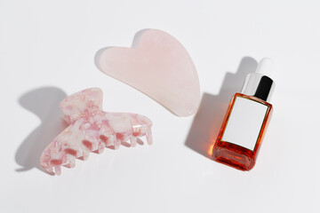 Gua Sha scrapes from rose quartz, hair Claws clip and serum vitamin C on white background. Beauty concept.