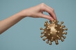 A woman's hand holds a gold-colored virus model. Blue background.