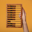 A woman's hand holds an old wooden abacus on a yellow background.