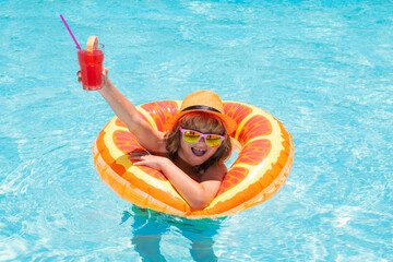 Wall Mural - Child in sunglasses and summer hat drink summer cocktail and floating in pool. Cute little boy in pool on summer day with tropical cocktail. Outdoor summer activity for children.