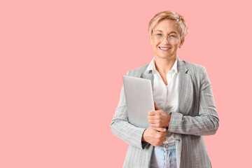 Mature female programmer with laptop on pink background