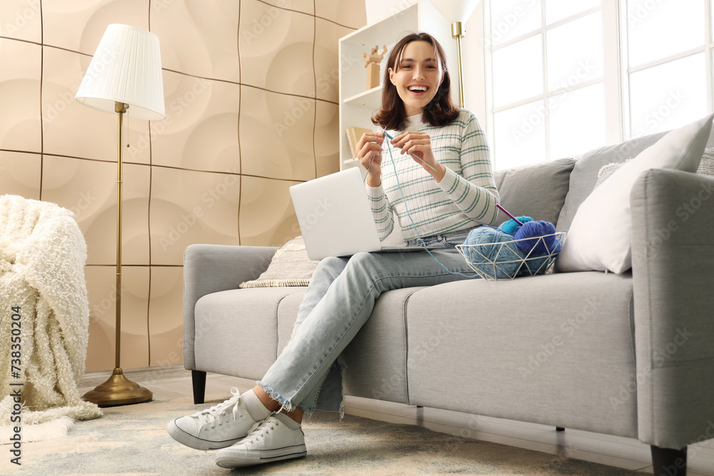 Young woman knitting with needles and laptop at home
