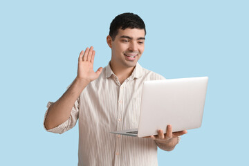 Wall Mural - Happy young man with laptop video chatting on blue background