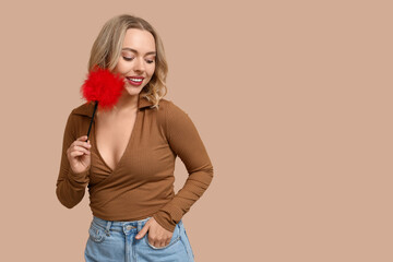 Wall Mural - Beautiful young woman with feather stick on beige background