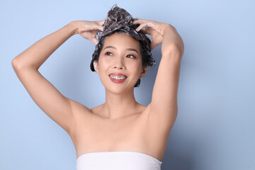 Poster - Young Asian woman applying shampoo on blue background, closeup