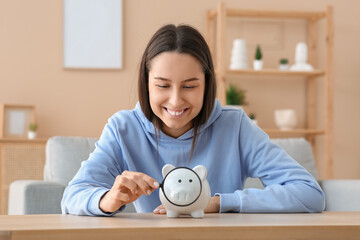 Wall Mural - Pretty young woman with piggy bank and magnifying glass at home