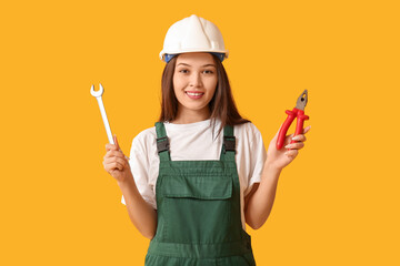 Sticker - Young female worker with wrench and pliers on yellow background