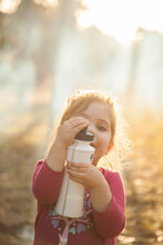 Little Girl Holding A Drink Bottle In Afternoon Sunlight With Campfire Smoke Behind