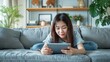 © Евгений Федоров - Asian woman lying on the couch using tablet at home in the living room. Digital downtime: Asian woman enjoying her tablet.