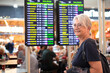 © luciano - Woman traveler - senior lady standing inside airport terminal looking at timetable schedule. Travel and transportation themed image.