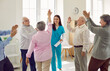 Group of happy lively joyful senior people having fun at retirement home. Good friendly smiling young nurse in uniform with clipboard gives high five to old woman while other patients applaud