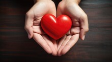 Human Hands Presenting A Glossy Red Heart On A Dark Wooden Background.