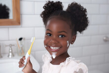 Funny Dental Hygiene Scene Of A Happy Black Girl Child Smile After Brushing Her Teeth In The Morning With Electric Toothbrush, Foam On Smiling Face, In Bathroom With Copy Space On White Wall Tiles