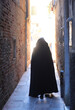 anonymous hooded stroller with black cloak dress walking through the narrow alleys