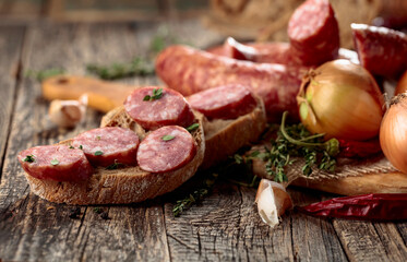 Dry-cured sausage with bread and spices on a old wooden table.