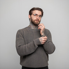 Wall Mural - Beautiful fashion male studio portrait of handsome business man with hairstyle and tattoos with sunglasses in vintage stylish knitted gray sweater on a white background