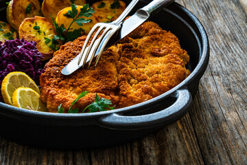 Wall Mural - Crispy breaded fried cutlet with baked potatoes and cooked red cabbage on wooden table
