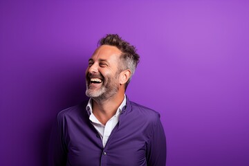 Wall Mural - Portrait of a happy mature man laughing and looking at the camera on a purple background