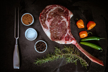 Wagyu tomahawk steak on a slate background with salt, pepper, rosemary and peppers