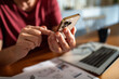 © Marko Geber - Close-up of a man using a smartphone with a laptop and documents on the table