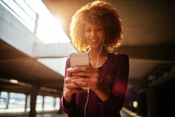 Young woman using a smart phone after jogging and exercising in a parking lot