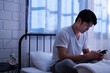 © MergeIdea - Asian teenager boy scroll mobile phone, search and online watching online movie after chat message and playing internet with his friend in bedroom of a dimly light