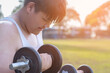 Young asian plump boy doing exercise with lifting heavy dumbbells in outdoor park in the sunset time of the day, sunlight edited.