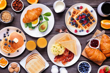 Wall Mural - Breakfast or brunch table scene on a dark wood background. Overhead view. Variety of sweet and savory food items.