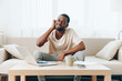 © SHOTPRIME STUDIO - Tired African American Man Working on Laptop in a Depressed State at Home on a Modern Sofa Unhappy Millennial Freelancer Experiencing a Crisis in Cyberspace