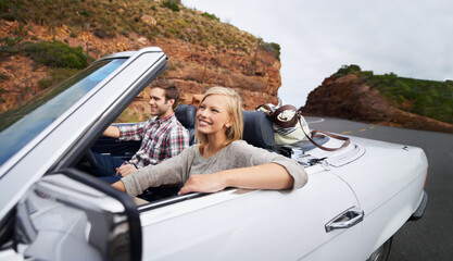 Wall Mural - Happy couple, car and driving on road trip for travel, holiday weekend or outdoor vacation on street in nature. Young man and woman with smile for transportation or getaway in convertible vehicle