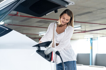 Young woman travel with EV electric car to shopping center parking lot charging in downtown city showing urban sustainability lifestyle by green clean rechargeable energy of electric vehicle innards