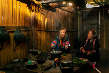 Asian family cooking and having dinner meal together at home. Hill tribe woman in traditional dress cooking food with herbal vegetable in traditional kitchen. Tribal culture and nature food concept.