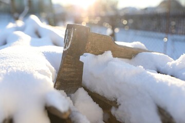 Wall Mural - Metal axe on snowy firewood outdoors on sunny winter day, closeup