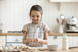Little adorable smiling girl in apron making dough, cooking pastries, prepare surprise for family on holiday in morning, stand alone in cozy kitchen. Hobby, cookery, homemade sweets recipe, vocation
