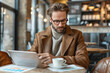© PHAISITSAWAN - Young entrepreneur analyzing digital financial charts on a tablet, coffee shop setting. AI Generated