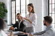 © fizkes - Experienced female manager sharing her point of view, providing feedback to subordinate workers and motivating employees. Young woman speaking out and coming up with suggestions during office meeting