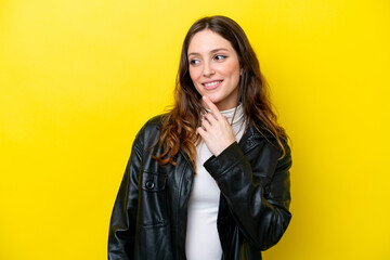 Wall Mural - Young caucasian woman isolated on yellow background looking up while smiling