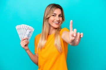 Wall Mural - Young Uruguayan woman taking a lot of money isolated on blue background showing and lifting a finger