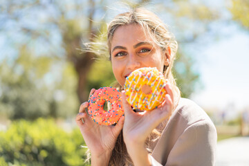 Poster - Young pretty blonde Uruguayan woman at outdoors holding donuts with happy expression