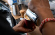 Close up of barista pouring hot frothy steamed milk into delicious golden flat white at local coffee shop