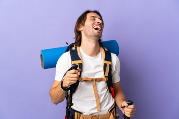 Young mountaineer man with a big backpack over isolated background laughing