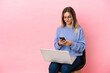 © luismolinero - Young woman sitting on a chair with laptop over isolated pink background sending a message with the mobile