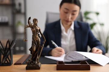 Canvas Print - Notary signing document at table in office, focus on Lady Justice statue