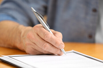 Wall Mural - Senior man signing Last Will and Testament at wooden table, closeup