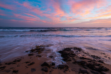 Wall Mural - Colorful clouds over the beach shore at sunrise time.