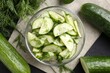 Cut cucumber with dill in glass bowl and fresh vegetables on table, flat lay