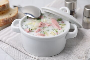 Delicious cold summer soup (okroshka) with boiled sausage in pot and spoon on white table