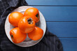 Delicious ripe persimmons on blue wooden table, top view. Space for text